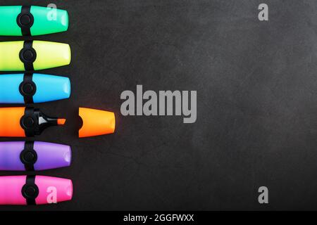 Multi-colored markers in a row on a black background, top view. The concept of creativity and study time Stock Photo