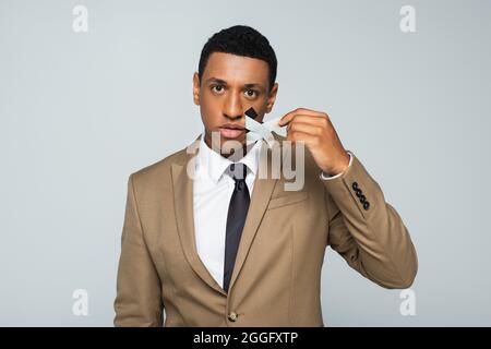 african american businessman taking off scotch tape on mouth isolated on grey Stock Photo