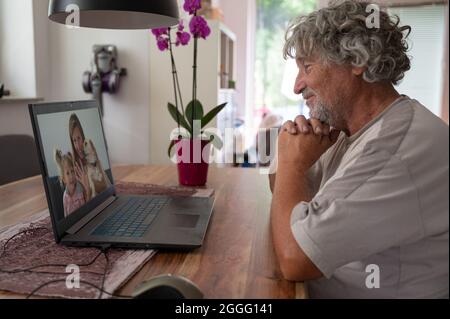 Grandpa talking to his family - daughter and granddaughter, via online meeting using laptop computer. Stock Photo