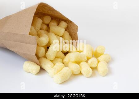 heap of sweet crunchy corn sticks or snacks in small paper bag isolated on white background, side view Stock Photo