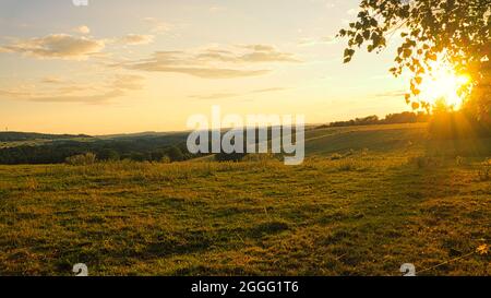 hilly landscape in the saarland. sunset on a meadow with view into the valley. interesting light atmosphere, colorful and beautiful Stock Photo