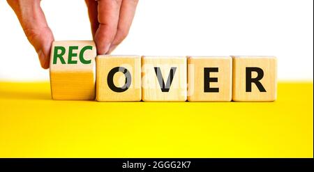 Time to recover symbol. Businessman turns a wooden cube and changes the word 'over' to 'recover'. Beautiful yellow table, white background. Business, Stock Photo