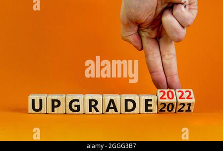 Symbol of planning 2022 upgrade new year. Businessman turns a wooden cube and changes words 'upgrade 2021' to 'upgrade 2022'. Beautiful orange backgro Stock Photo