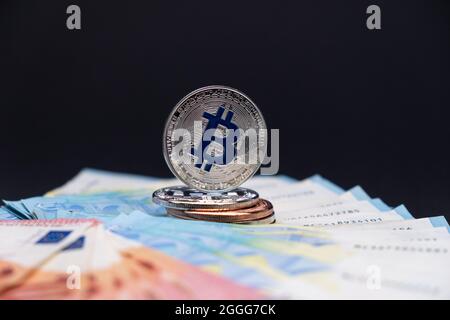 Bitcoins with blue symbol in focus lies on top of 20 and 10 Euros bank notes. Bitcoins on ten and twenty euros banknotes on dark background. Stock Photo