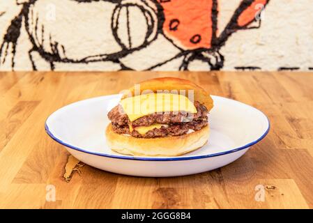 Double beef burger with melted cheddar cheese and brioche bread on a white enamel plate Stock Photo