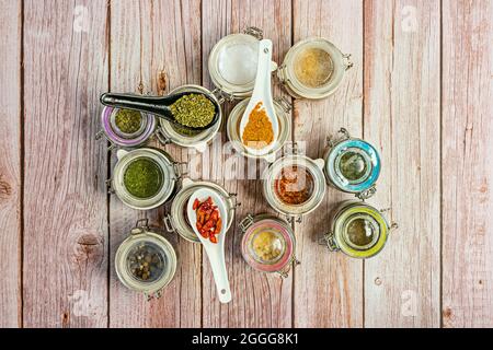 Transparent glass jars with assorted spices seen from the top with some spoons with yellow curry, small cayenne and oregano. Sea salt flakes, white pe Stock Photo