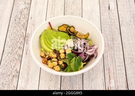 Vegetable salad with coriander, chopped ripe avocado, red onion, roasted cucumbers, whole hazelnuts and lettuce sprouts inside a bowl for home deliver Stock Photo