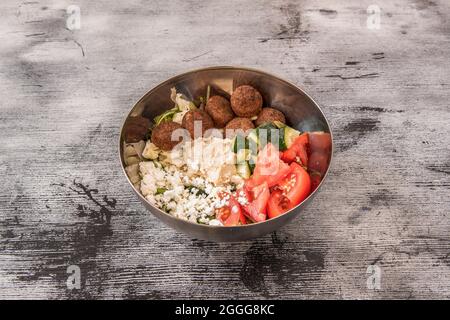 Bowl with salad of tomatoes, cucumbers, lettuce and crumbled cheese with falafel croquettes and a little hummus. Stock Photo