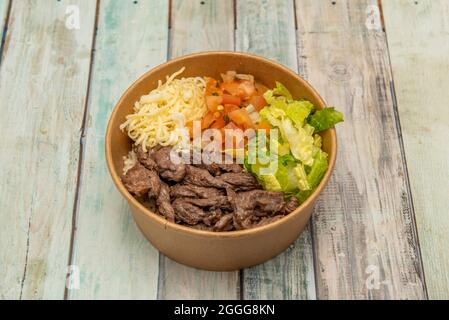 bowl of stewed beef with pieces of tomato and onion, parsley, grated cheese and lettuce in a takeaway container Stock Photo