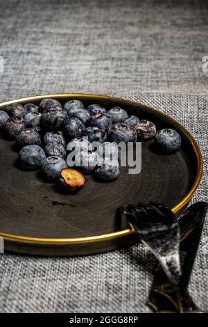 Image with focus on the well-ripe blueberries that are inside a black plate with a golden rim Stock Photo