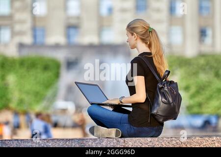 Remote work by woman with laptop in city garden. Stock Photo