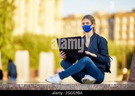Woman in protective medical mask with laptop works outdoors. Stock Photo