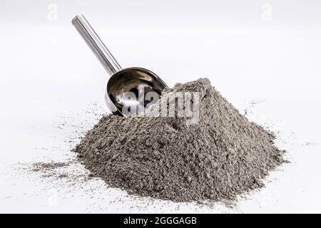Cement powder pile on isolated white background with metal measuring spoon. Stock Photo