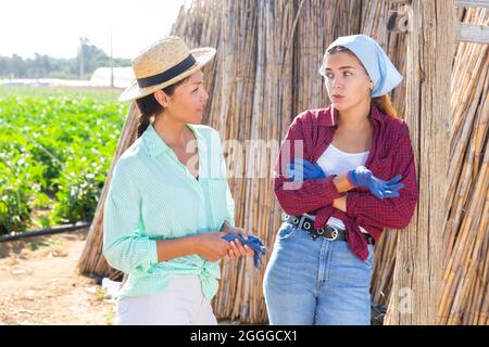 Asian woman farmer talking friendly to her young female companion in farm Stock Photo
