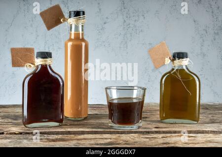 Bottles and glass with handmade liquor on wooden table with empty labels . Artisan Alcoholic drinks. horizontal Stock Photo