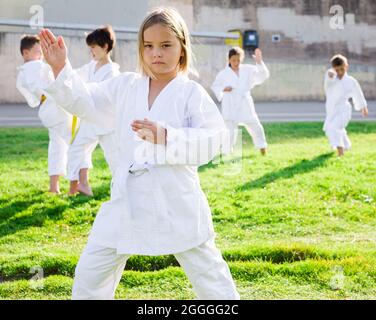 Little girl in white kimono training karate in park Stock Photo