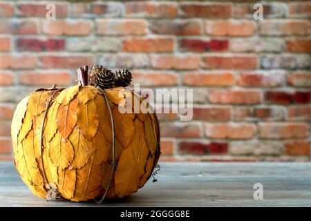 Decorative pumpkin made of yellow leafs isolated against red brick wall background. Thanksgiving concept Stock Photo