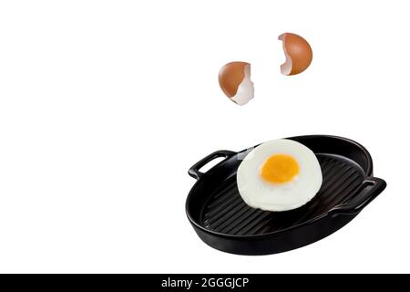 An image of an egg being cracked, falling, and transforming to fried egg on a black ceramic serving pan. Levitation food concept. Stock Photo