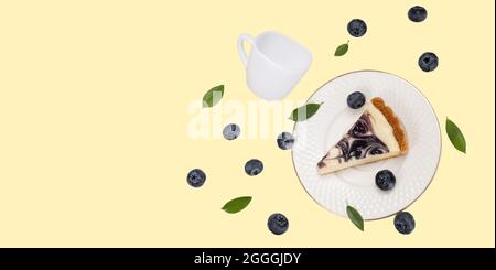 A piece of blueberries cheesecake on a falling white  ceramic plate with falling white ceramic cup and some flesh bleuberries and green leaves on soft Stock Photo
