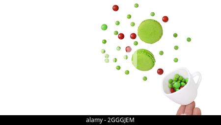 A hand spilling a cup of red and green chocolate candies and pieces of green pistachio macaroons. Food levitation photography concept. Isolation on wh Stock Photo