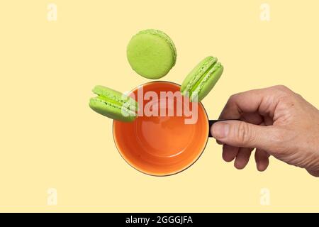 A hand holding an ornage mug with falling pieces of pistachio macaroons. Stock Photo
