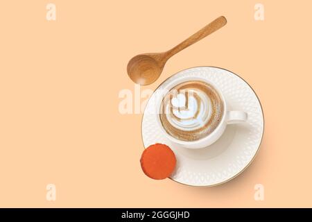 A white porcelain cup with cappuccino coffee and a gold rimmed saucer with a wooden spoon and an orange macaroon levitating. Stock Photo