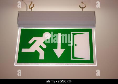 Green evacuation direction sign on ceiling. Emergency exit sign with running man on it. Stock Photo