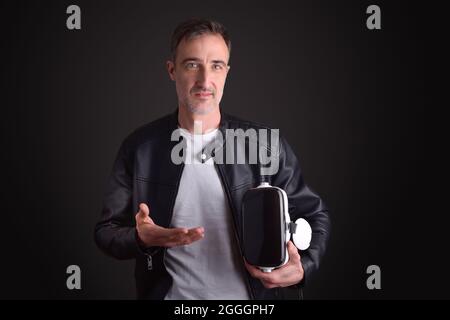 Man showing virtual reality headset dressed in white t-shirt and black leather jacket on black isolated background Stock Photo