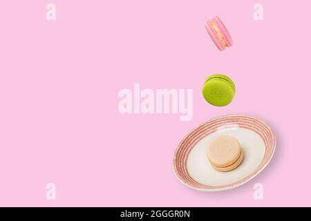 Colorful macaroons floating on a ceramic plate. Beautiful soft pink background. Lavitation food concept. Stock Photo