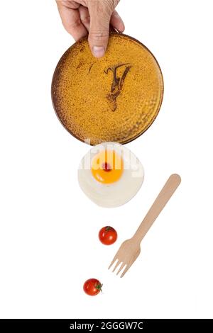 A hand holding a ceramic dinner plate with falling fried egg and red cherry tomatoes. Levitation food photography concept. Stock Photo