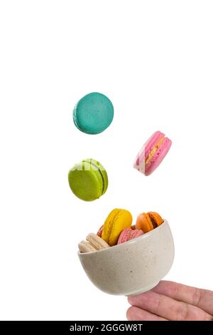 Colorful macaroons floating on a ceramic bowl with a hand holding its base with finger tips..  Isolation on white background. Food levitation concept. Stock Photo