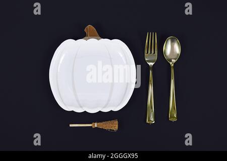 Halloween party pumpkin shaped plate, brooms and golden fork and spoon on black background Stock Photo