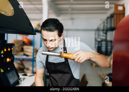 Handsome man in apron looking at freshly roasted coffee beans while standing by coffee roasting machine. Stock Photo