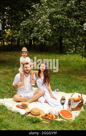 Stock photo of beautiful young family in white at picnic in the park. Loving mother in white dress kissing her son in lips. Little boy kissing his mot Stock Photo