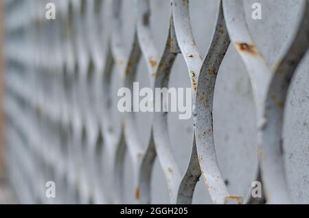 The metal honeycomb against the gray concrete in the receding perspective. An old rusted iron wall or fence. Architecture. Selective focus. Stock Photo