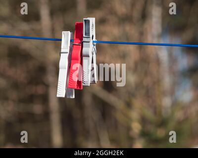 Three plastic cloths pegs, red white and gray attached to a washing line in a garden. Close up, selective focus. Stock Photo