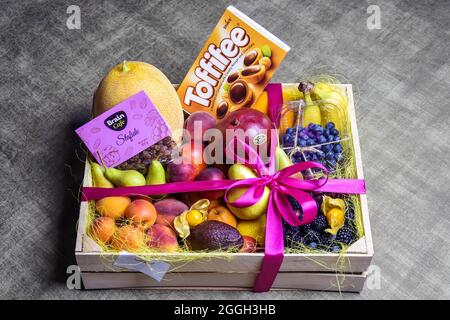 Moldova, Chisinau - July 2021: Variety of ripe fruits and berries are beautifully stacked in wooden box tied with pink ribbon. Dark background. Food d Stock Photo