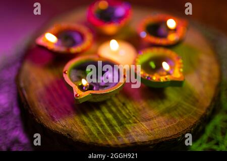 Four lit candles in small decorative clay pots and tea light candle burning on round wooden board Stock Photo