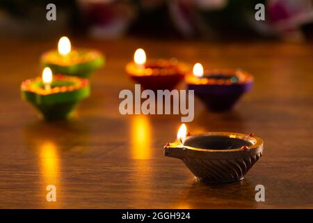 Four lit candles in small decorative clay pots burning on wooden table top Stock Photo