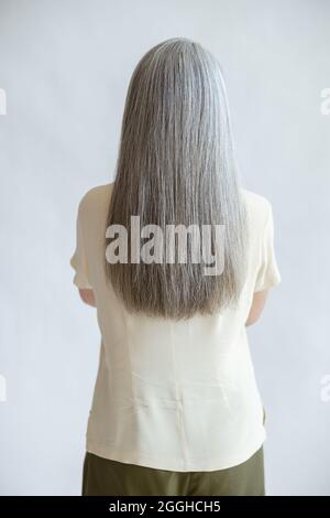 Lady with long loose silver hair stands on light grey background Stock Photo