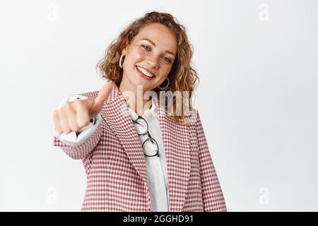 Happy businesswoman shows thumbs up and smiles pleased, praising your work, complimenting, like something good and recommending, white background Stock Photo