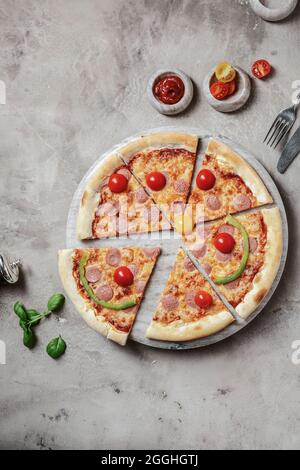 Tasty pizza with  sausage, mozzarella for children with smiley  on marble round tray. Garnished on grey stone backdrop with pizza ingredients Stock Photo