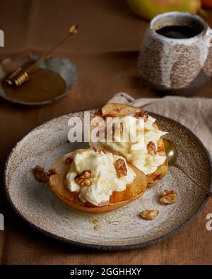 Sweet rustic dessert. Roasted pears with cream and nuts on wooden background. Honey and coffee Stock Photo