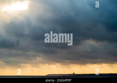 English seaside resort town of Margate bathed in sunbeams coming out of a very dark cloud in the early morning. Low horizon with offshore wind farm. Stock Photo