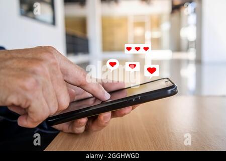 Man hand using smartphone with heart icon at office, He look message from lovers. Stock Photo