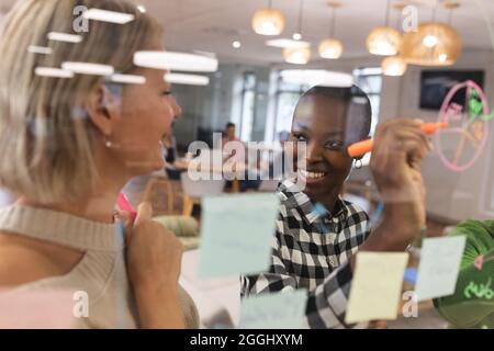 Smiling diverse female colleagues working together, brainstorming, writing on memo notes Stock Photo
