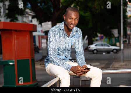 handsome adult african man sitting in the street using his mobile phone Stock Photo