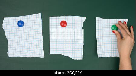 female hand attaches blank sheets of paper in a cage to a green magnetic board, place for an inscription Stock Photo