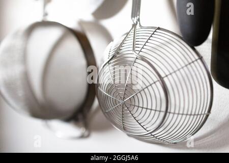 Close-Up of Metal Strainer Hanging on White Kitchen Wall Stock Photo