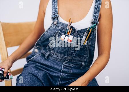 Brushes and paints in the pocket of denim overalls Stock Photo